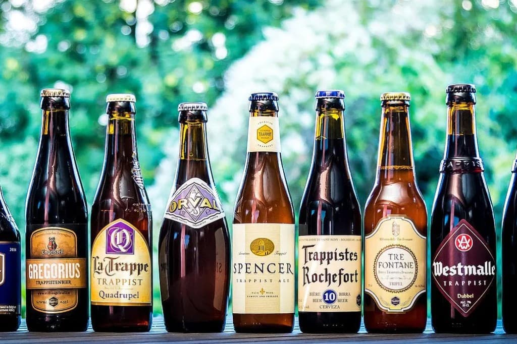 緑のボケ背景の前に並んだ、さまざまなトラピストビールなどの瓶ビール